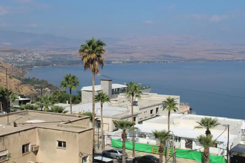 Aerial view of the Tiberias cityscape and the Sea of Galilee, Israel, with palm trees and hills beyond.
